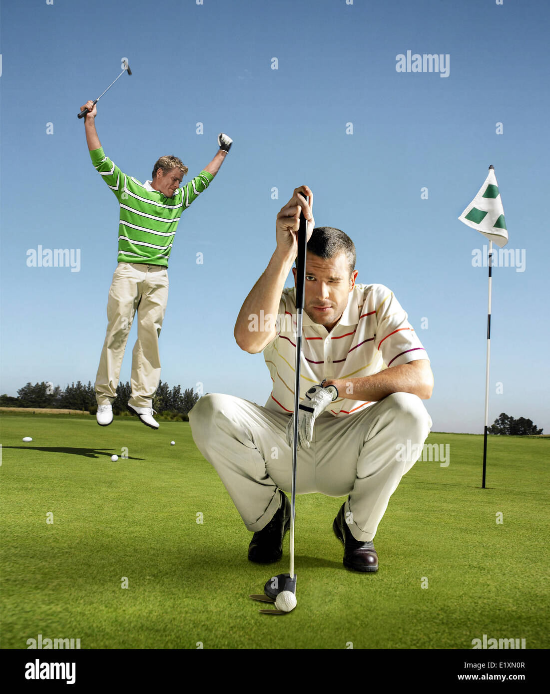 Full length portrait of golfer lining up shot with man jumping in background Stock Photo