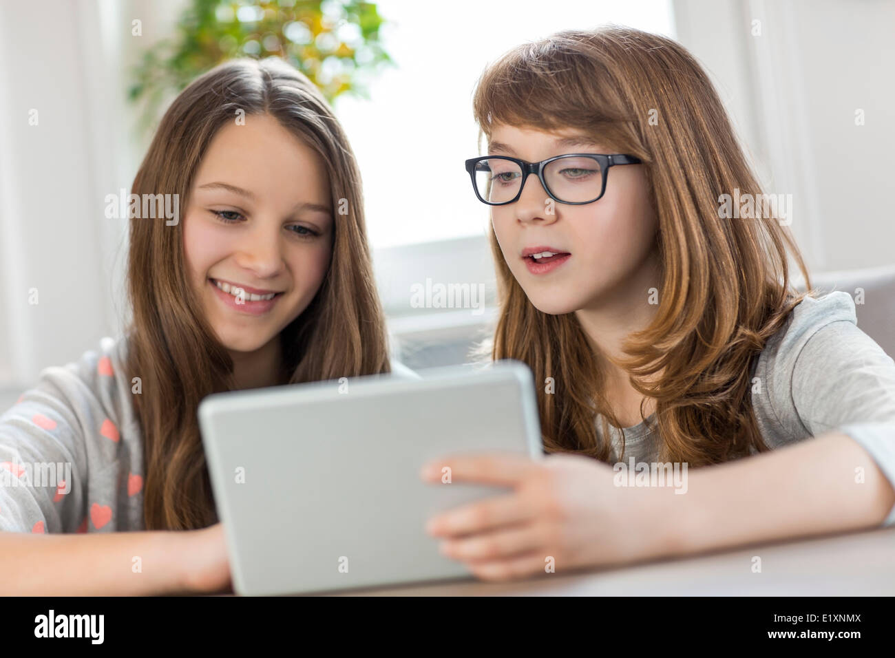 Sisters using digital tablet at table in house Stock Photo - Alamy
