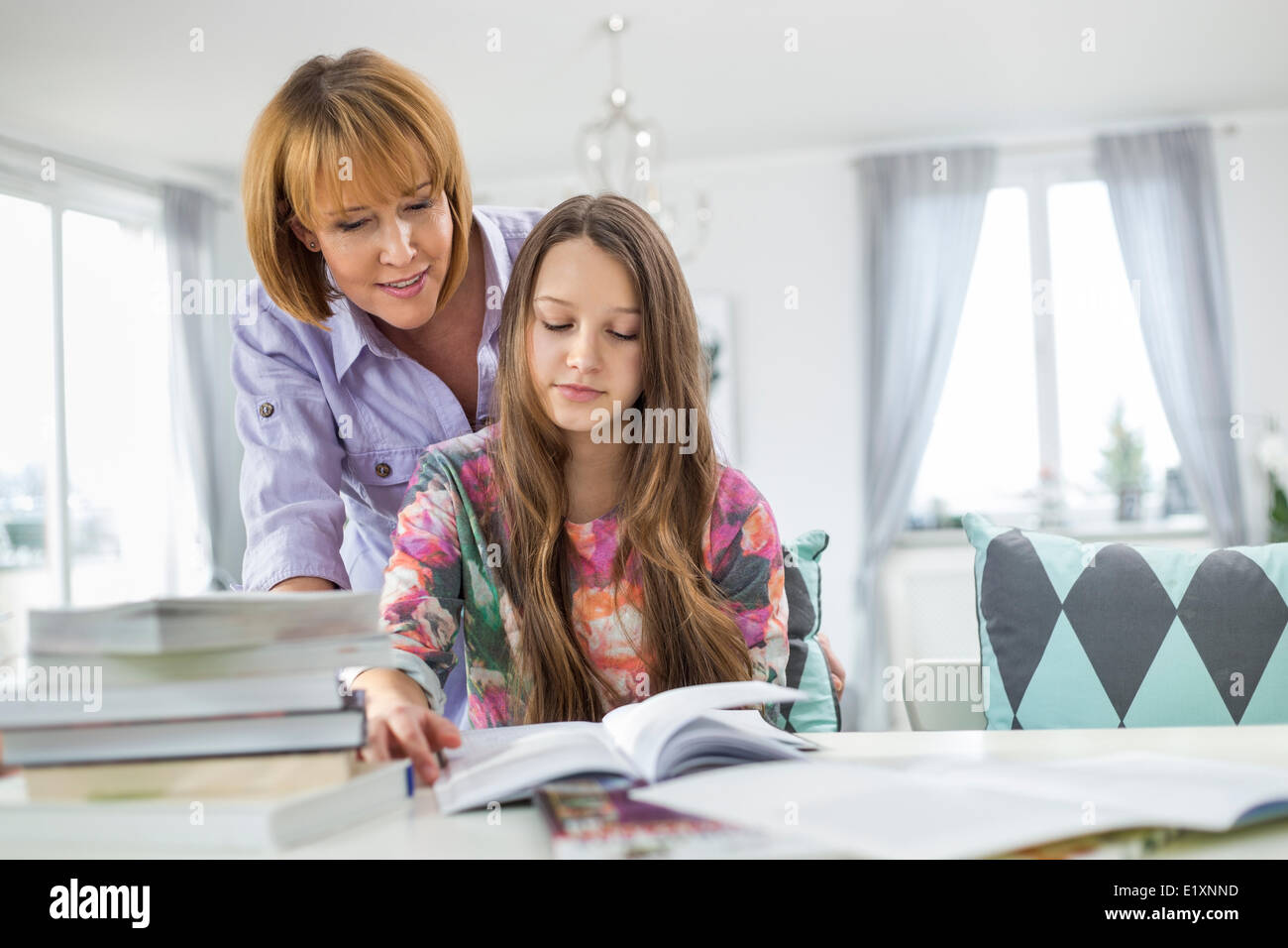 Mother assisting daughter in doing homework at table Stock Photo