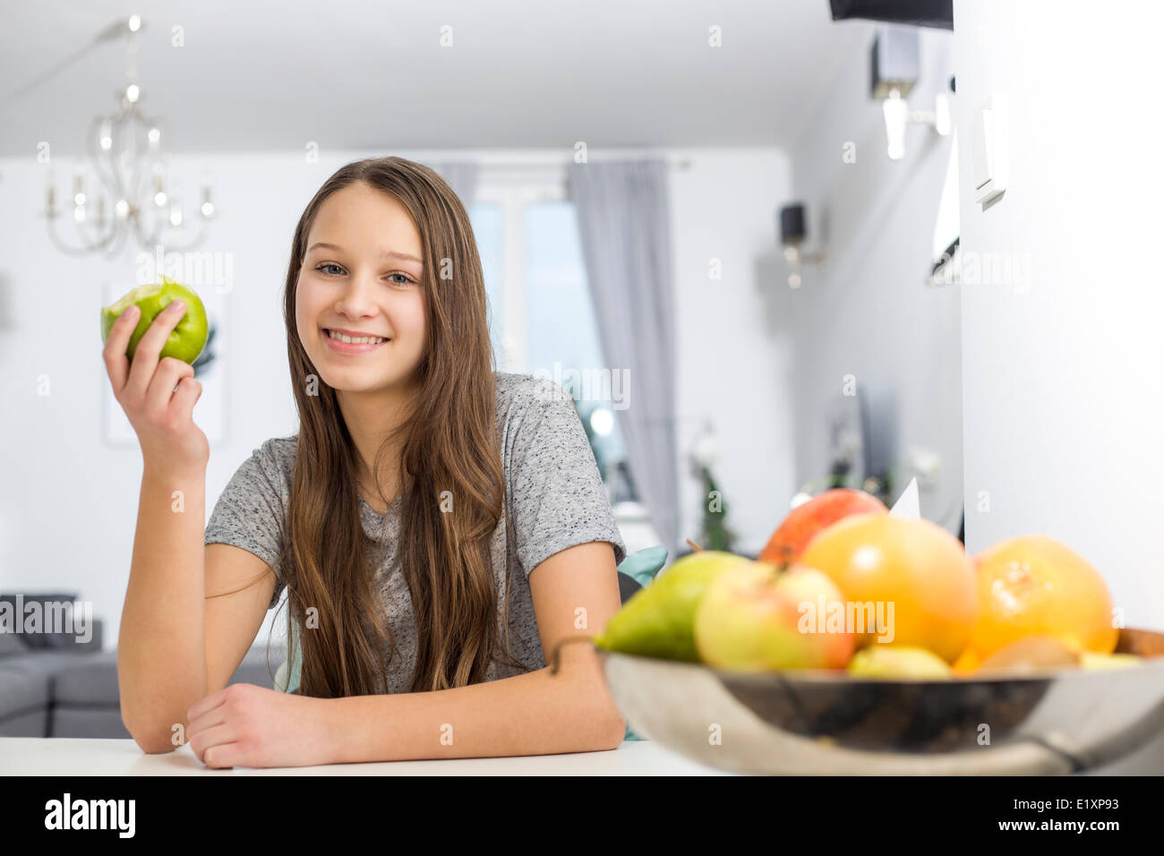 Portrait of smiling girl holding apple while sitting at table in house Stock Photo