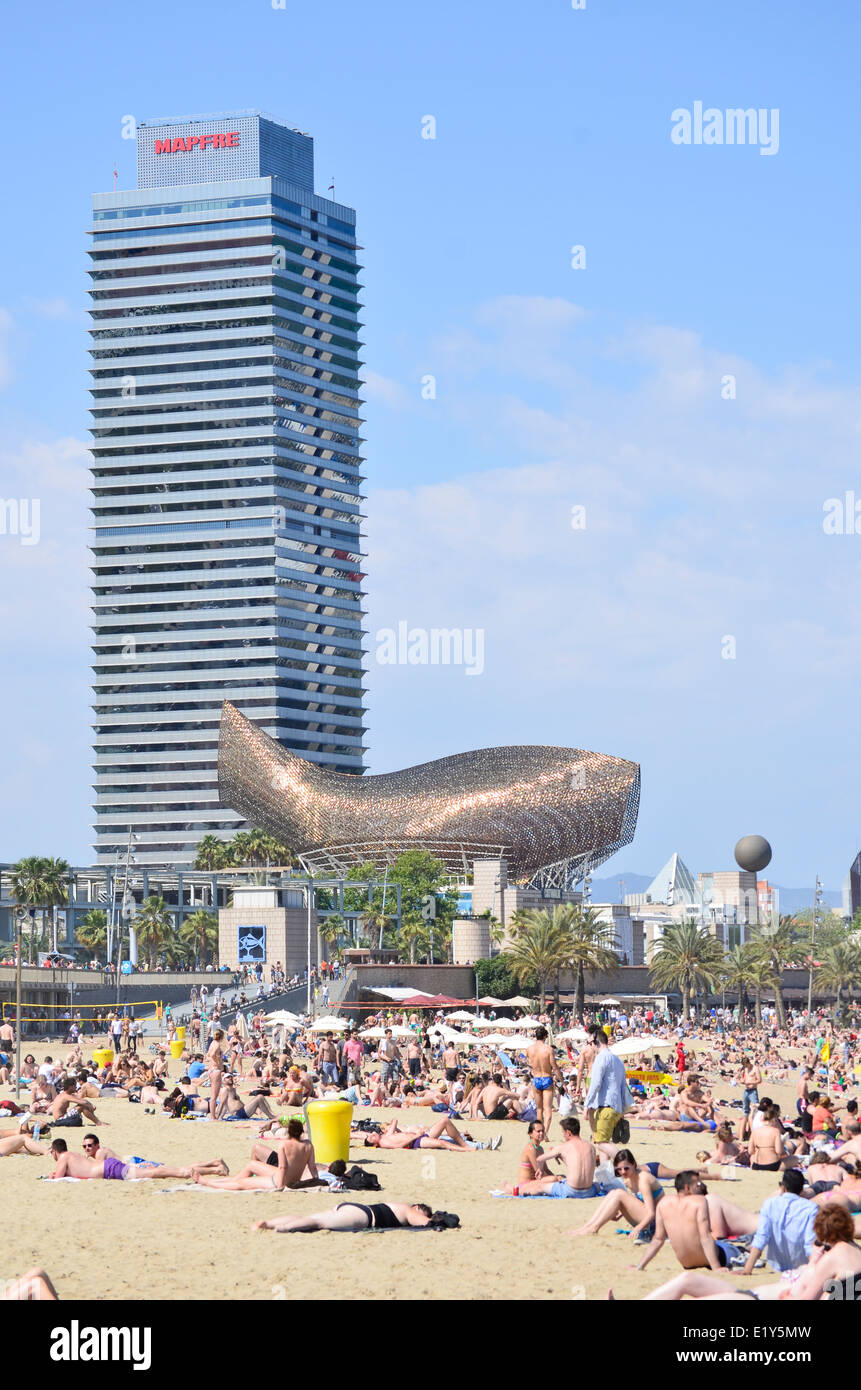 Sunbathers at Barceloneta Beach with Frank Gehry's Fish, Peix, Sculpture and Mapfre Tower Building. Barcelona, Catalonia, Spain. Stock Photo