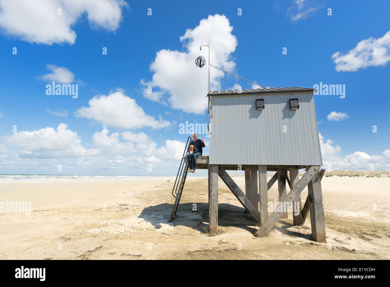 Man sitting with dog at drowning house at the beach from Dutch wadden island Terschelling Stock Photo