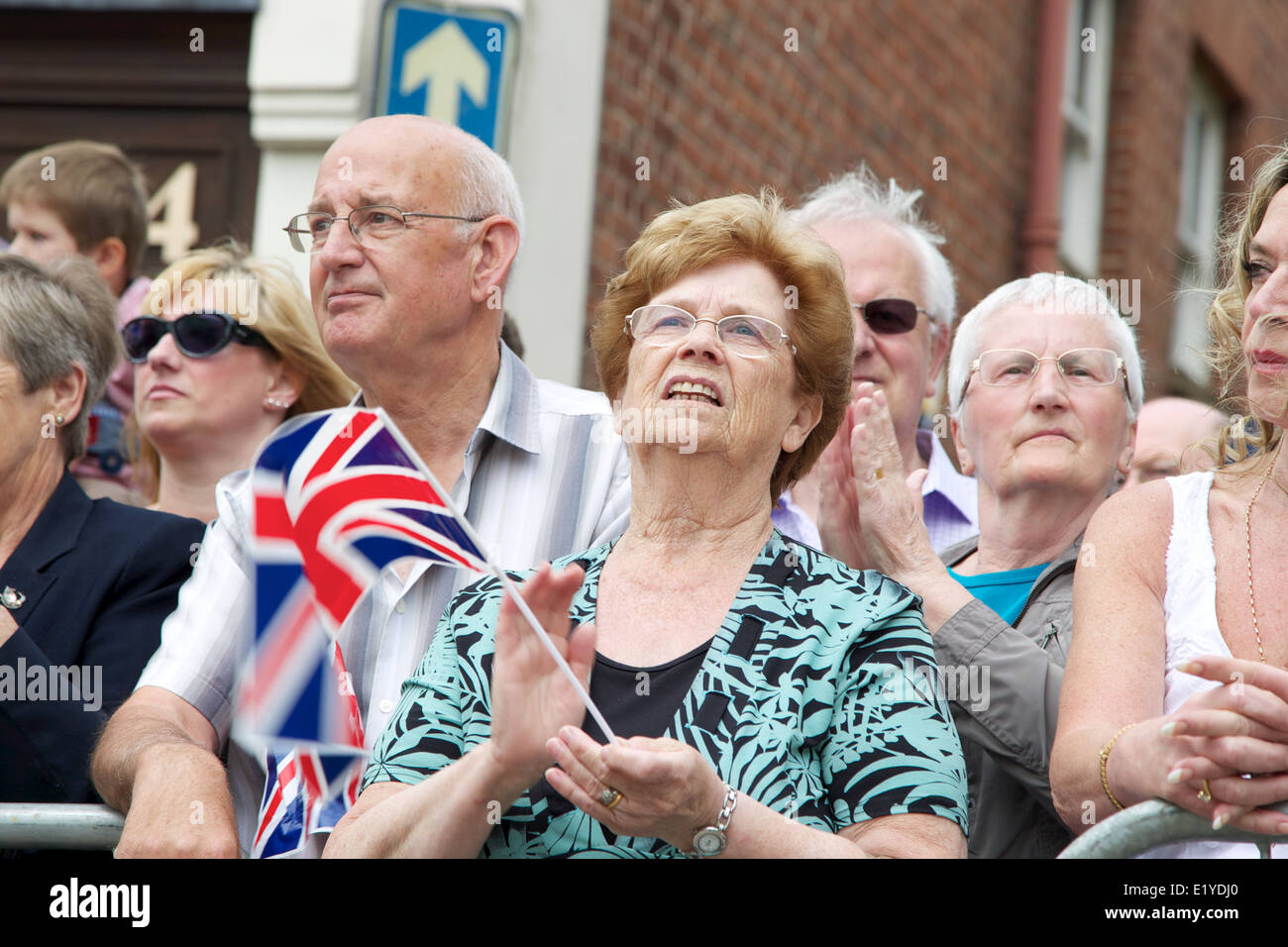 people lining the streets of warwick to wave union jack flags at a military parade Stock Photo