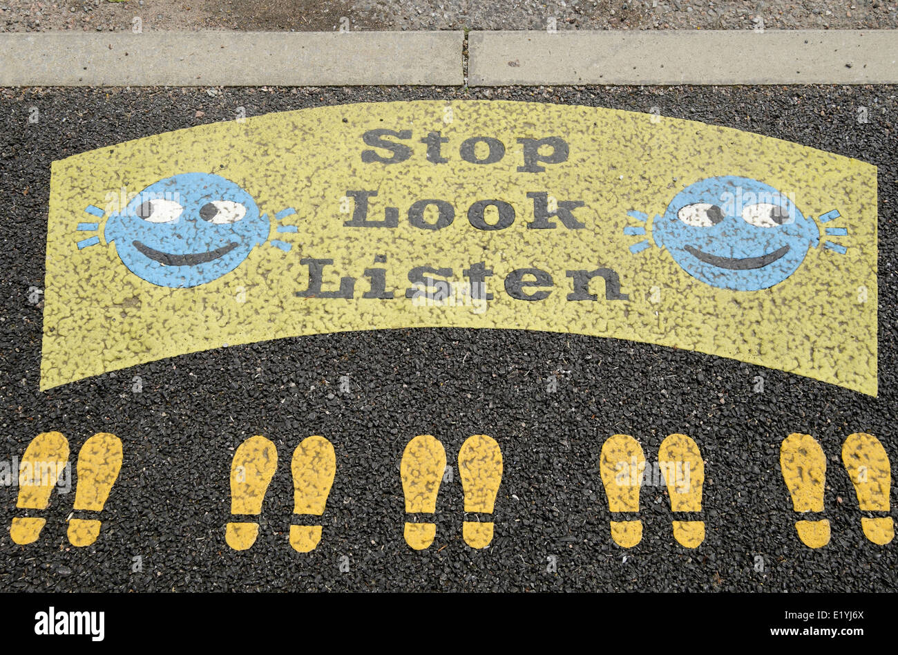 Stop Look Listen sign with smiley faces and footprints painted on a roadside kerb near a primary school road crossing from above. UK Britain Stock Photo