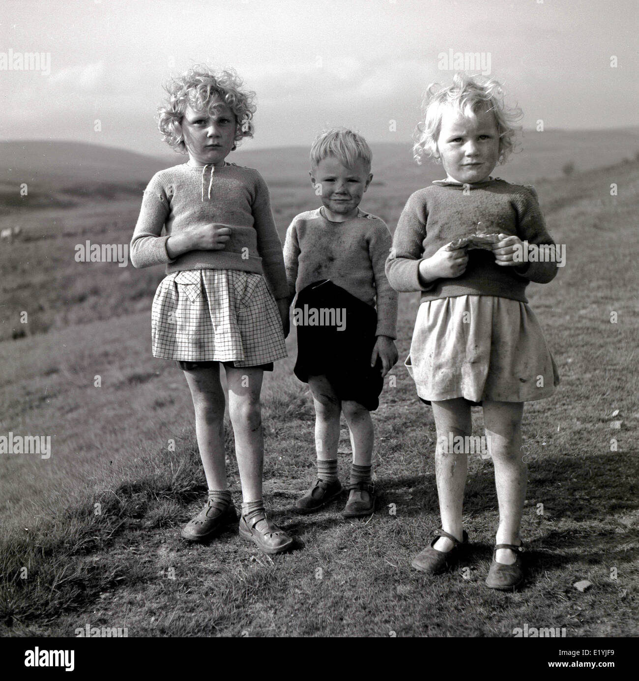 1950s historical portrait by J Allan Cash of three young country children standing together on a grassy hill. Stock Photo