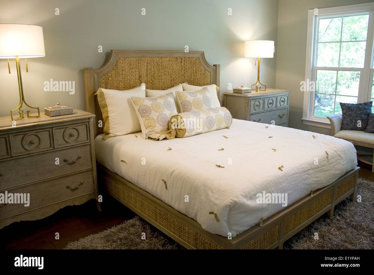 Elegant well lighted bedroom with dresser chest, lamps and headboard. Stock Photo