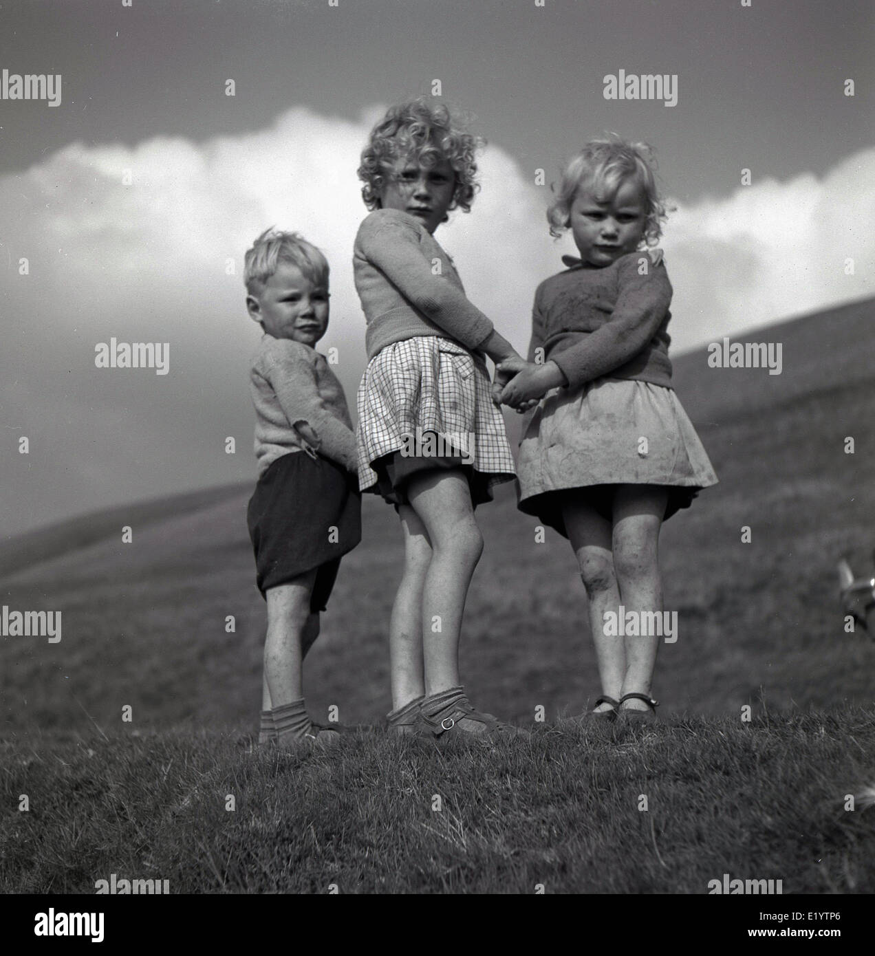 1950s, an historical portrait by J Allan Cash of three young country children standing together on a hillside holding hands. Stock Photo