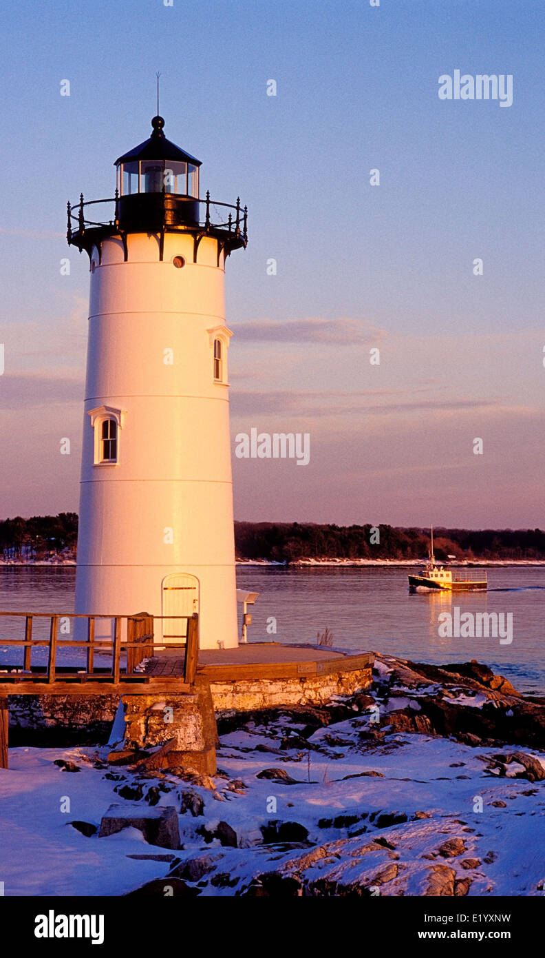 Portsmouth Harbor lighthouse guides a lobster boat home as the sun sets in winter. Stock Photo