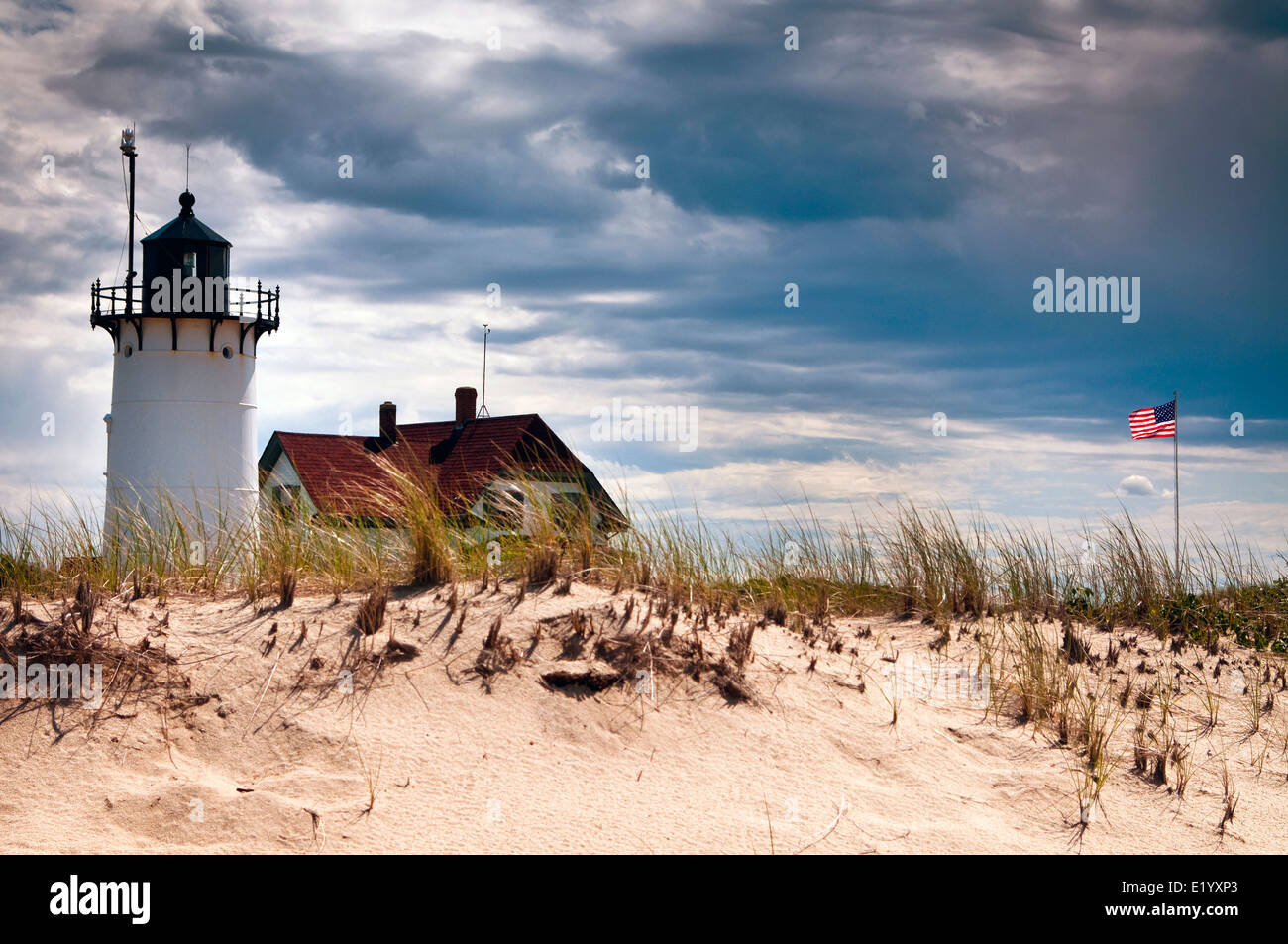 Summer storm clouds approach Race Point lighthouse as American flag waves nearby on Cape Cod, in Massachusetts. Stock Photo