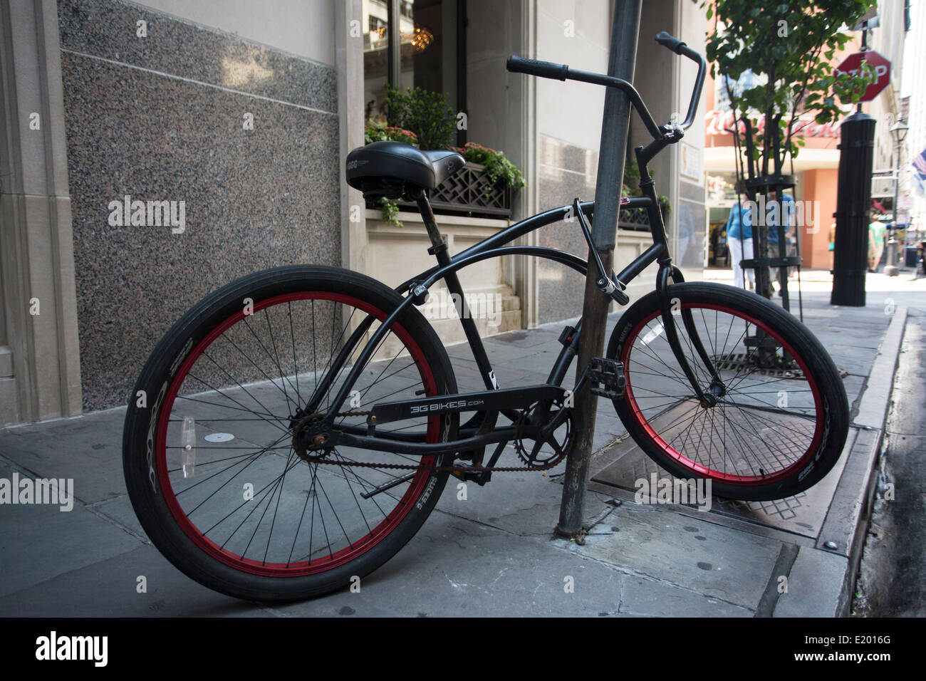 A black bicycle is locked to a pole on an urban street. Stock Photo