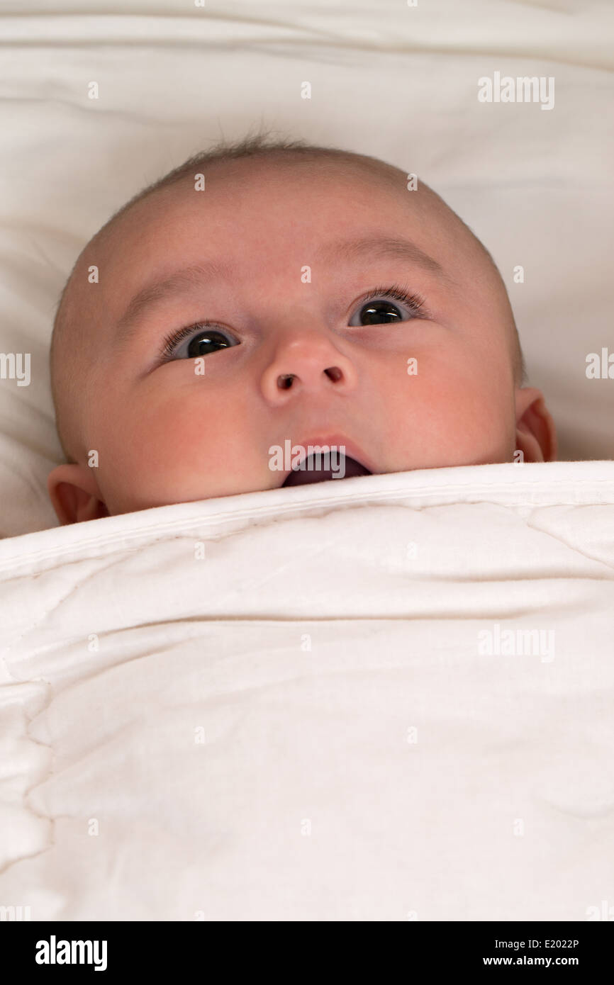 Baby is surprised with mouth open lying in bed Stock Photo