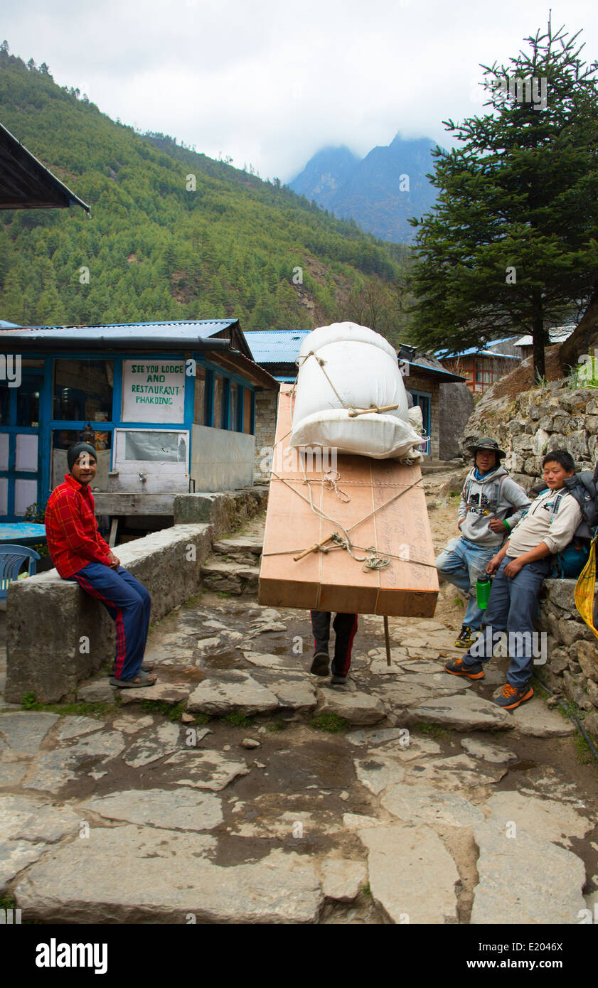 Nepal Himalayas Porter carrying massive load through the streets of Phak Ding Solukhumbu remote Mt Everest 55 56 Stock Photo