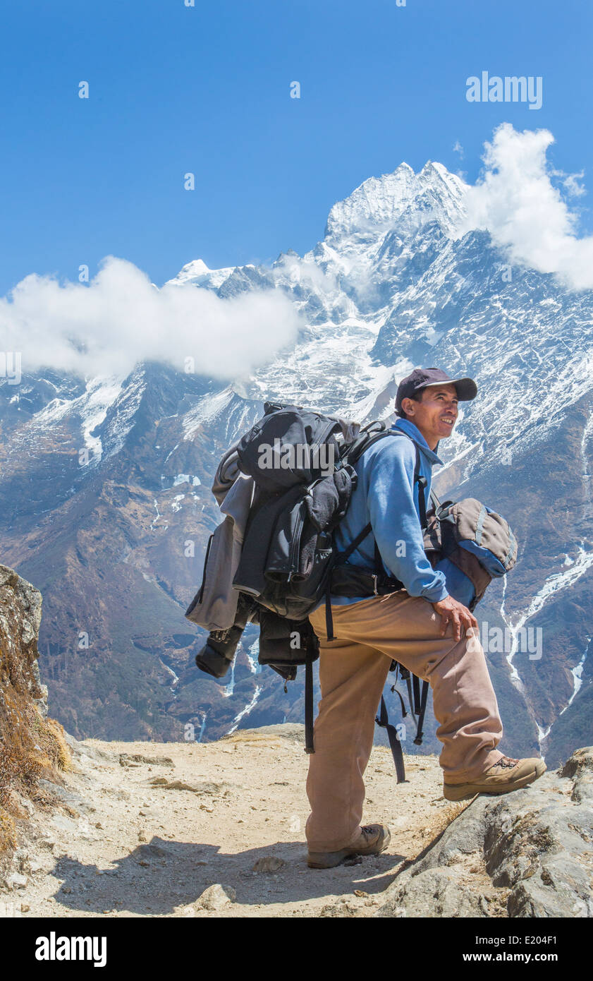 Nepal. Mountain Trekking guide poses with his bags and the Himalayan mountains in the distance. Solukhumbu, remote, Mt Everest, Stock Photo