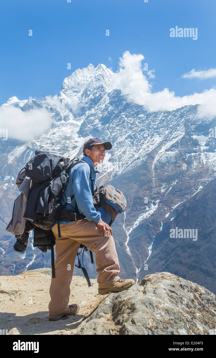 Nepal. Mountain Trekking guide poses with his bags and the Himalayan mountains in the distance. Solukhumbu, remote, Mt Everest, Stock Photo