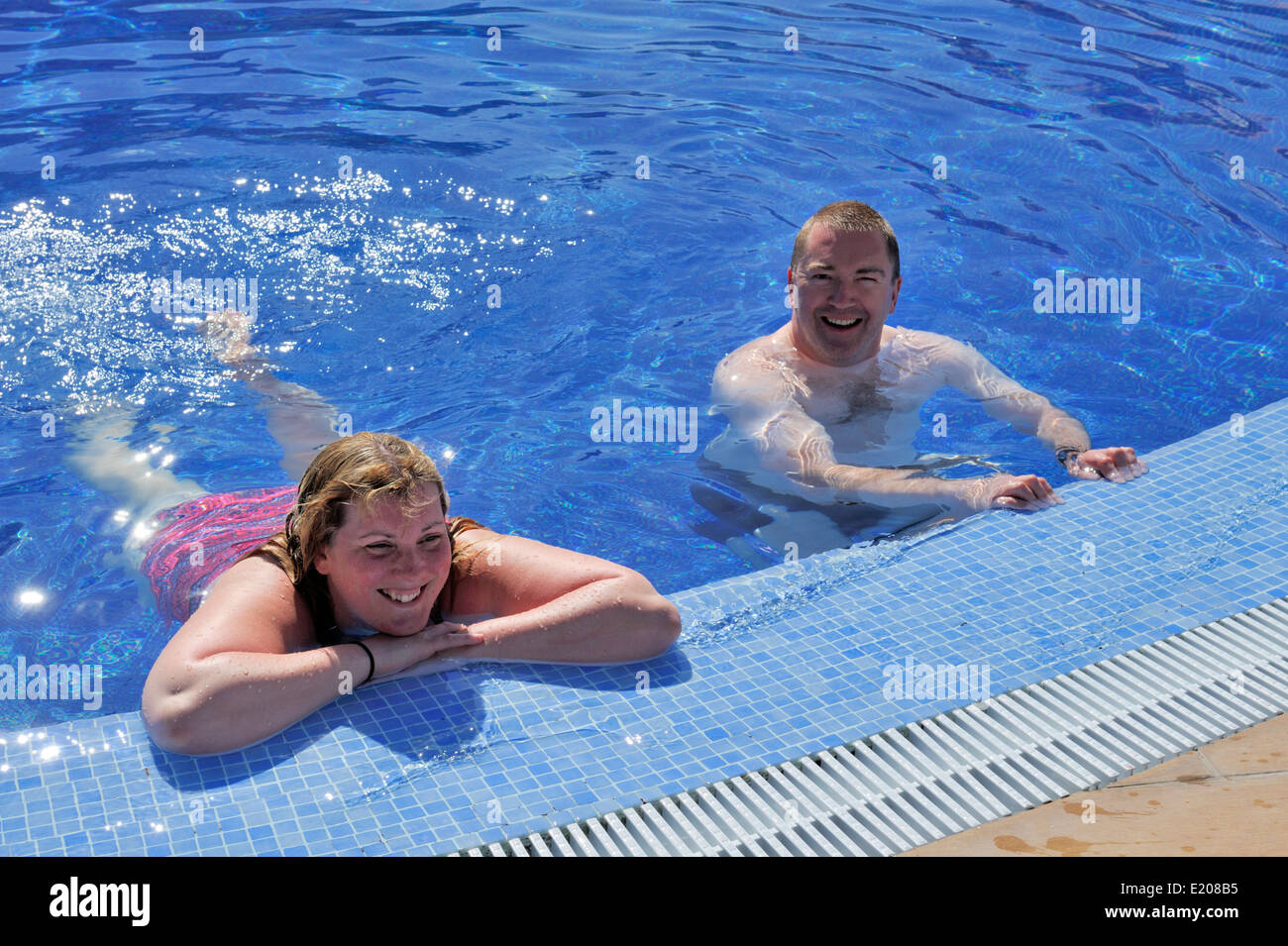 Two people in water by edge of swimming pool Stock Photo