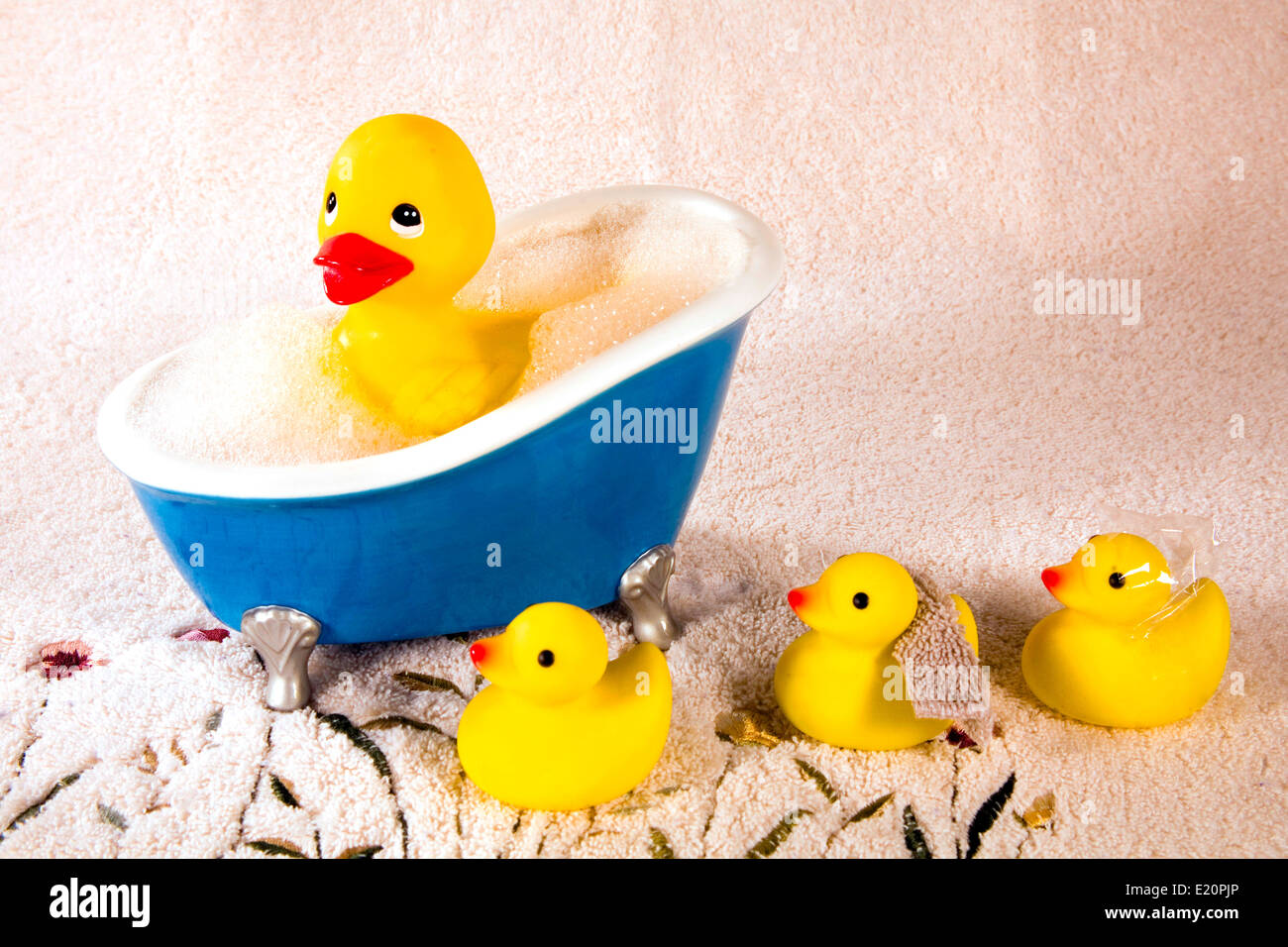Large rubber duckie in bubble bath with three smaller ducks waiting on a terry cloth towel. Stock Photo