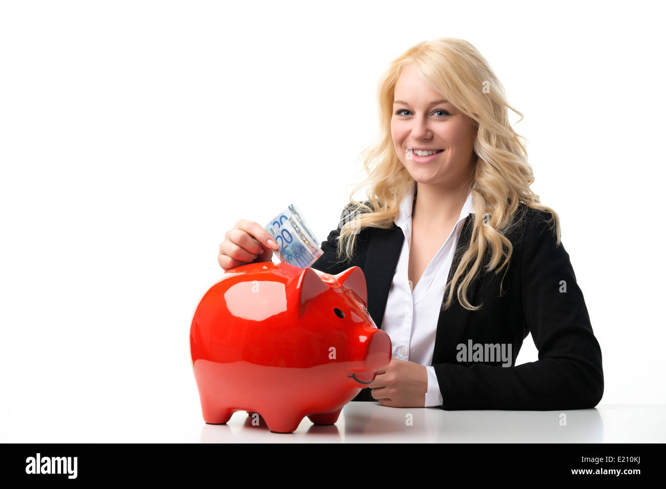 Happy blond women sitting at a table and throwing euro banknotes in a red piggy bank Stock Photo