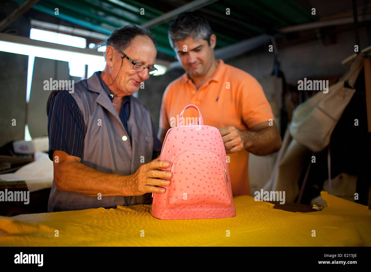 Elderly Italian father and middle aged son inspect a handmade leather bag in their workshop. Stock Photo