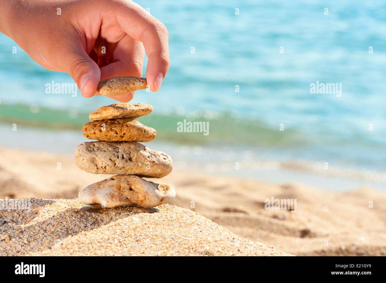 Stone tower on sand with hand against sea. Stock Photo