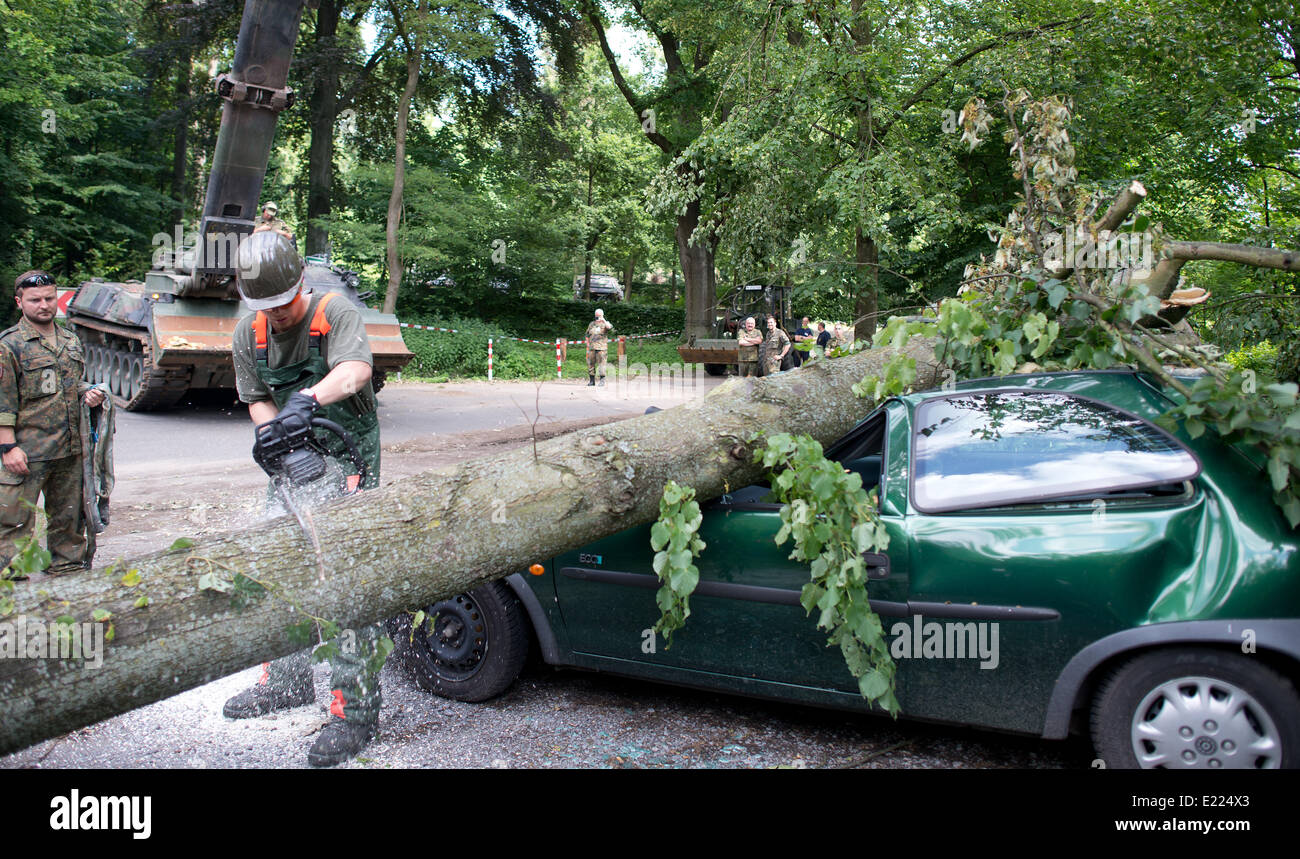 Duesseldorf, Germany. 13th June, 2014. A German Armed Forces soldiers saws up a tree which fell onto a car in Duesseldorf, Germany, 13 June 2014. About 300 soldiers of the German Armed Forces deployed on a clean-up operation with the help of two Armoured Recovery Vehicles among others after thunderstorms in North-Rhine Westphalia. Photo: FEDERICO GAMBARINI/dpa/Alamy Live News Stock Photo