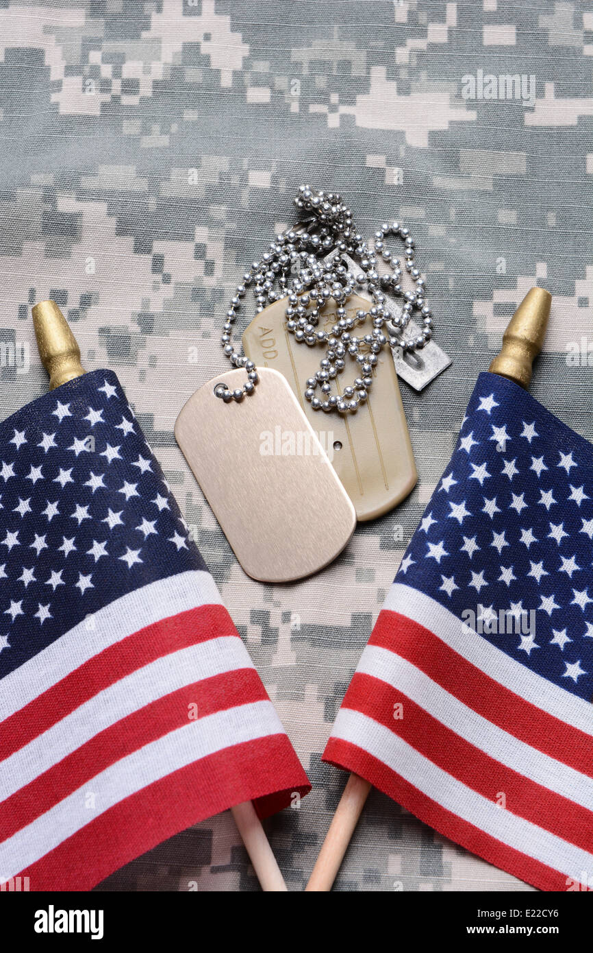 Closeup of two crossed American Flags on camouflage material with dog tags in the middle. Stock Photo