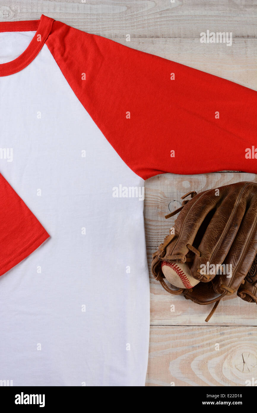 High angle shot of a baseball jersey with a ball and glove on wooden surface. Stock Photo