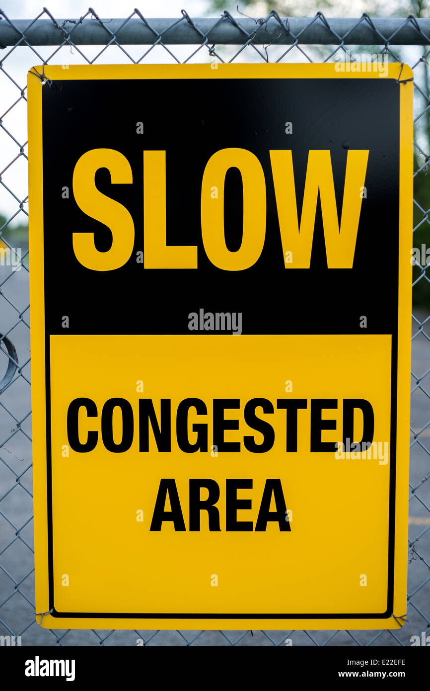 A yellow caution sign reading: Slow - Congested Area hanging on a chain-link fence Stock Photo