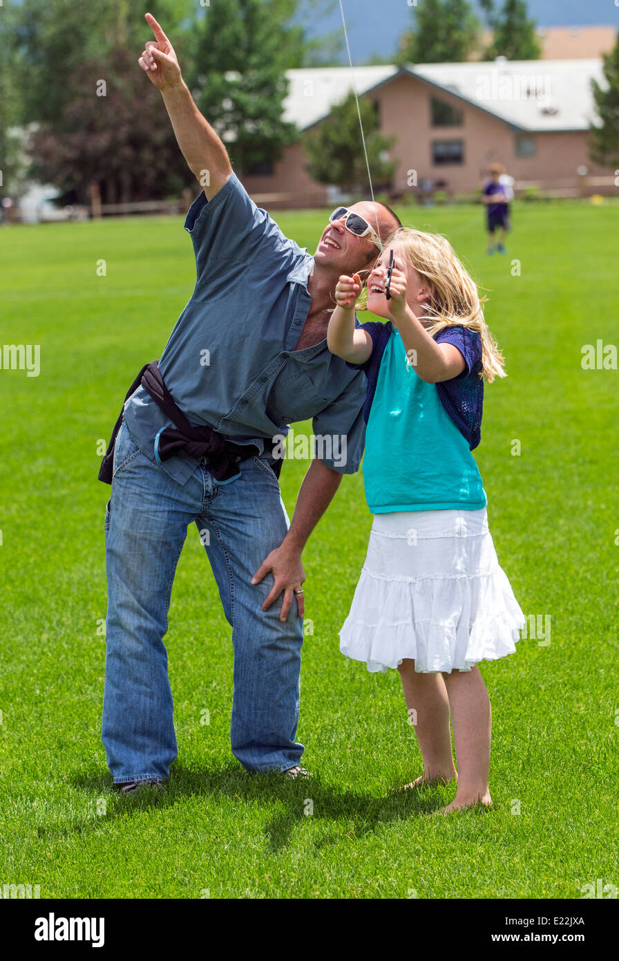 Father & young daughter flying a kite on a grassy field Stock Photo