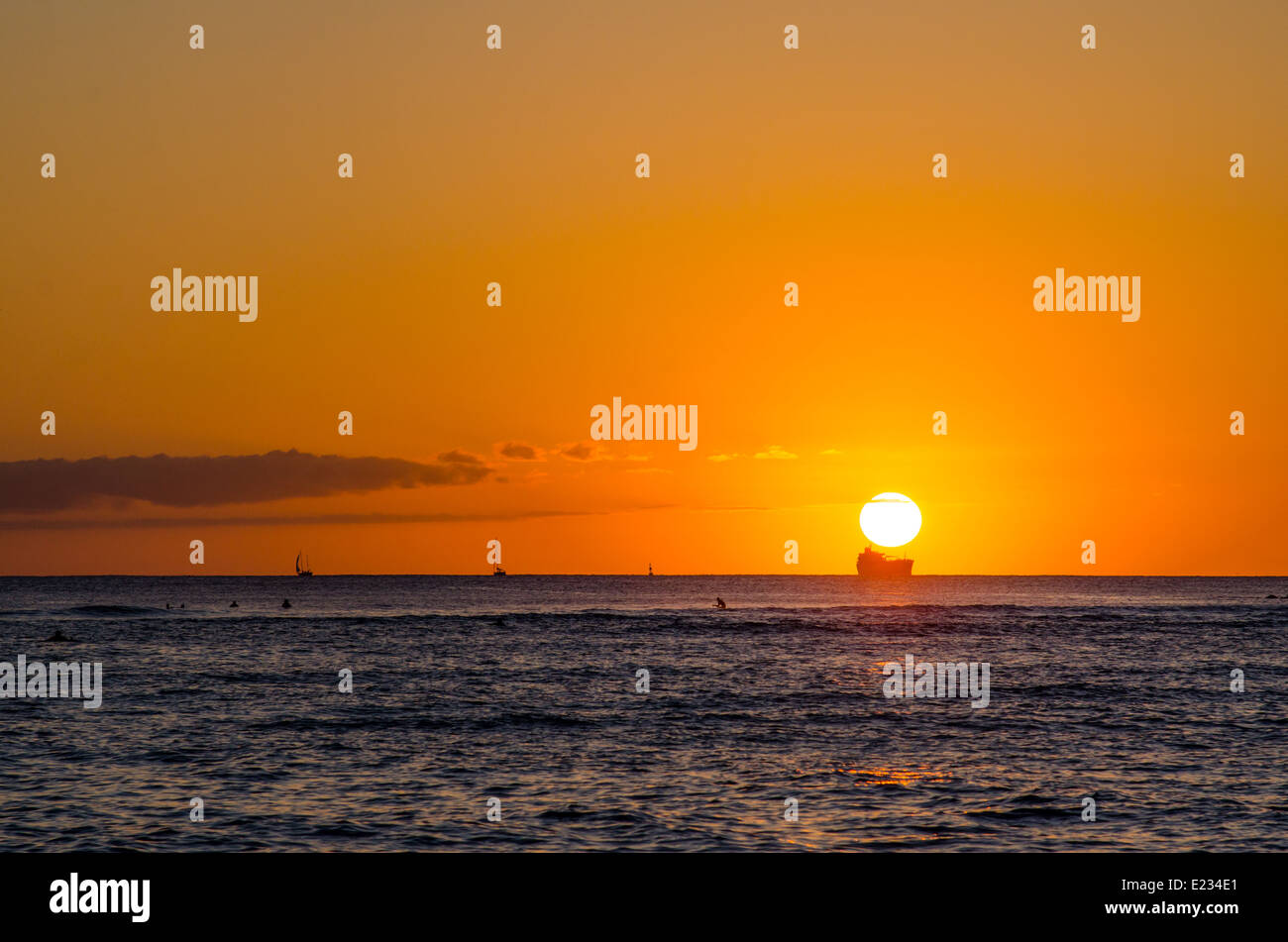 Sunset over the Pacific Ocean from Waikiki Beach in Hawaii, with a shipping tanker silhouetted against the setting sun Stock Photo