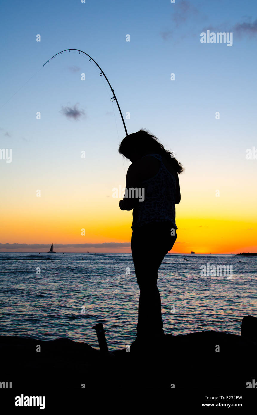 Silhouette of a young woman fishing at sunset on Waikiki Beach, Oahu, Hawaii. Stock Photo