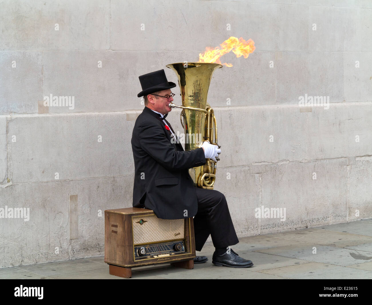 Busker, Christopher Werkowicz playing his flaming tuba sitting on an old radio against a plain stone wall London England Stock Photo