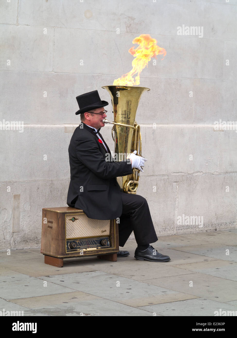 Busker, Christopher Werkowicz playing his flaming tuba sitting on an old radio against a plain stone wall London England Stock Photo