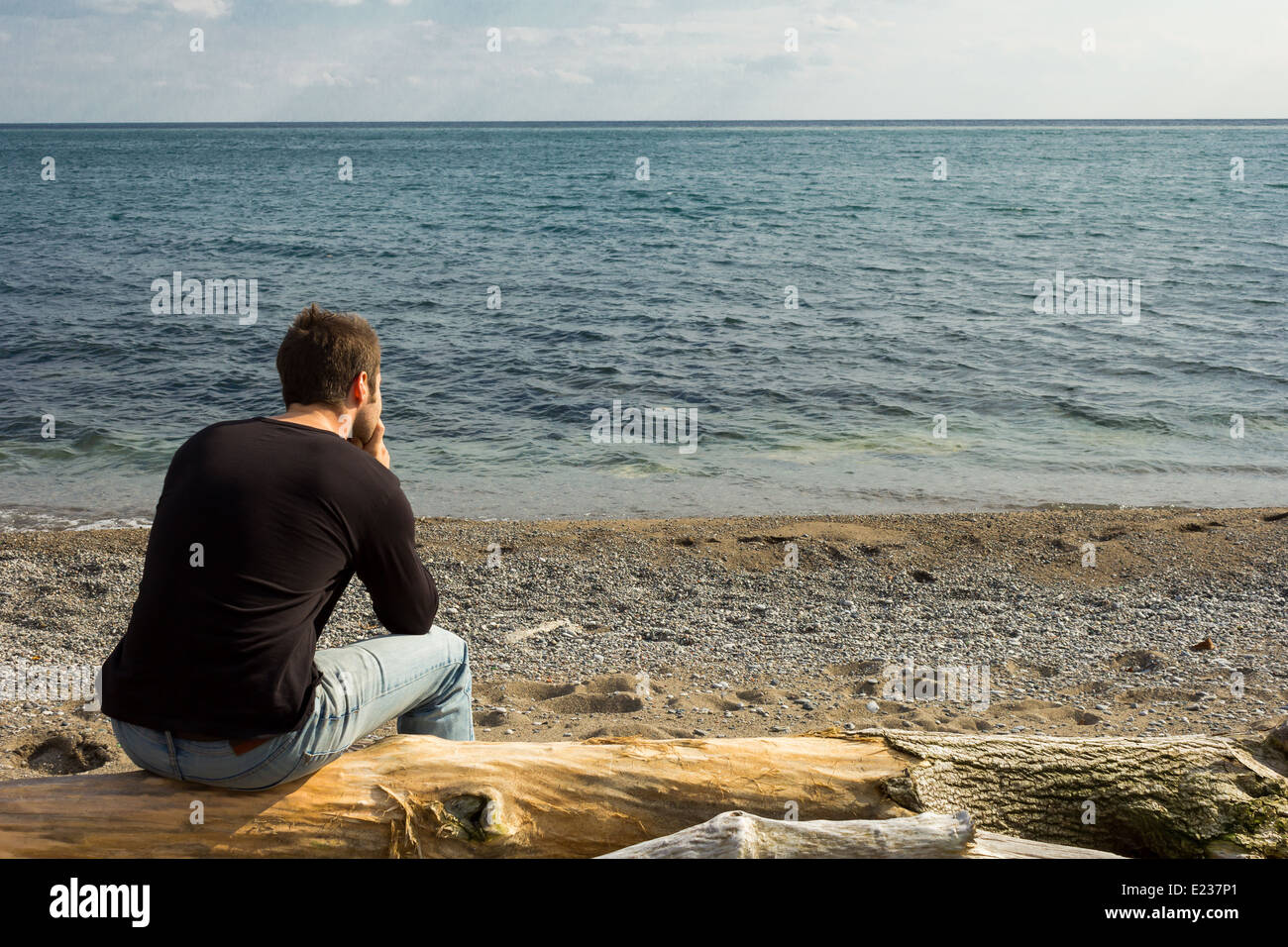 Man sitting on a log staring out to sea Stock Photo
