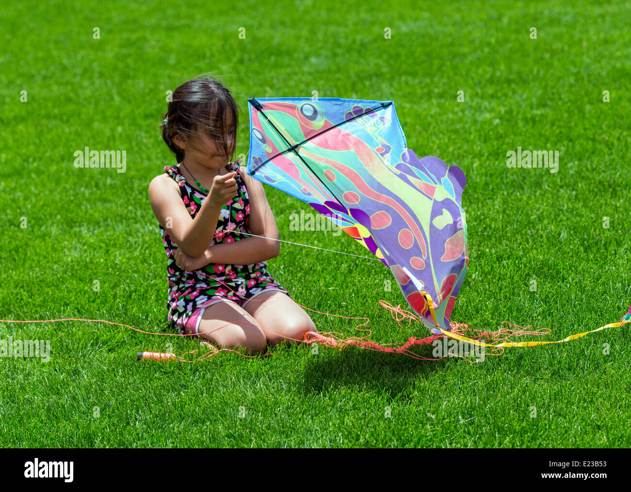 Young hispanic girl flying a kite on a grassy field Stock Photo