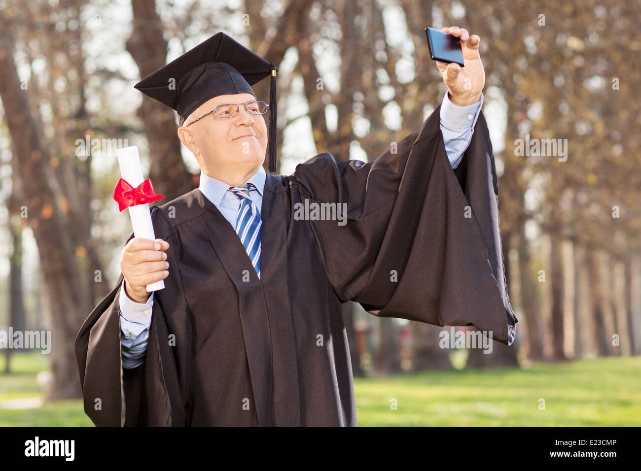 Mature man holding diploma and taking selfie in park Stock Photo