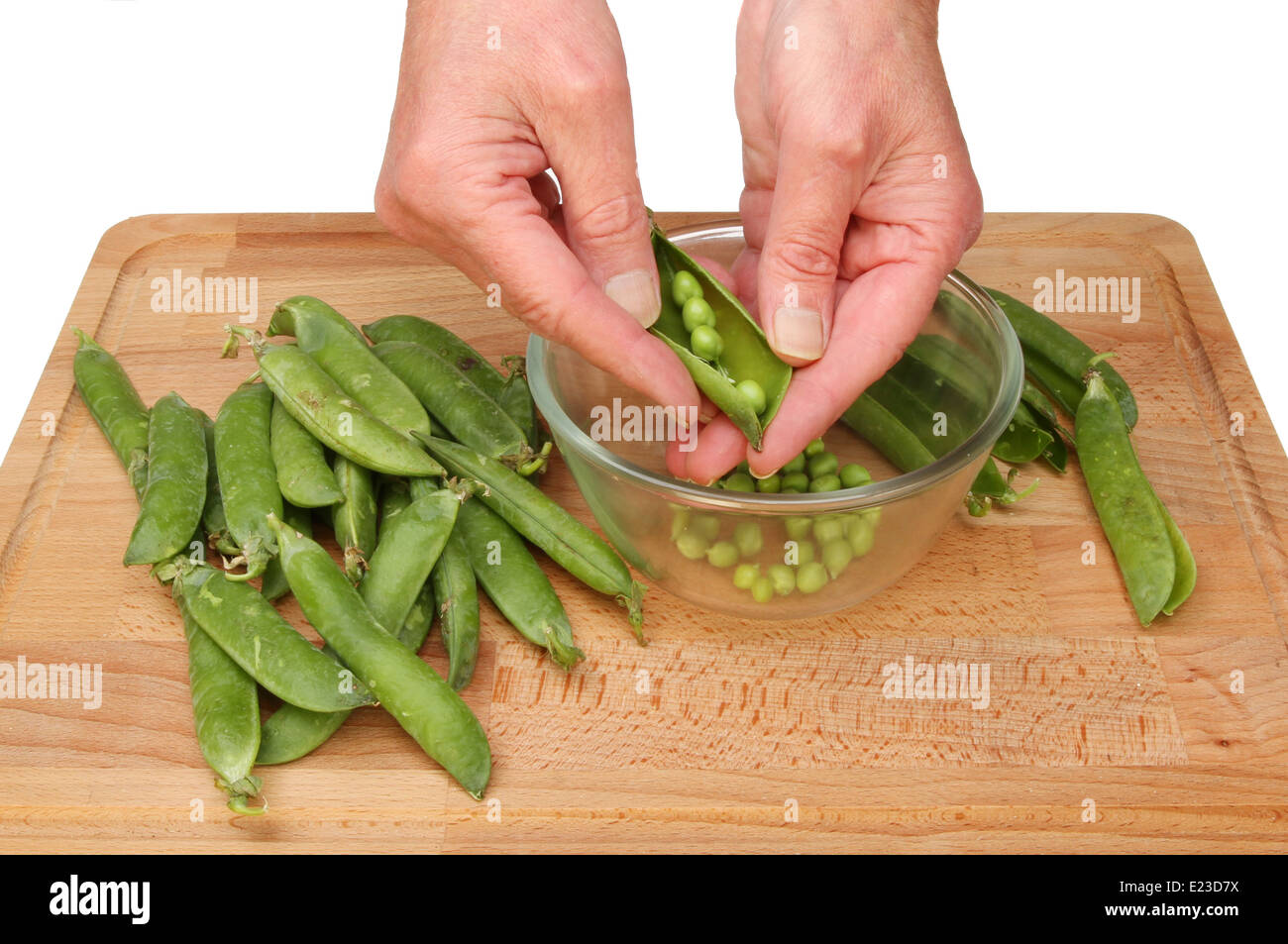 Hands shelling peas from pods into a glass bowl on a wooden board Stock Photo
