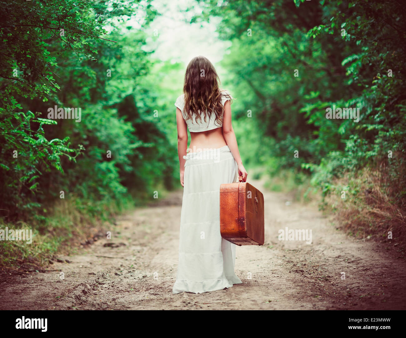 Young woman with suitcase in hand going away by a rural road Stock Photo