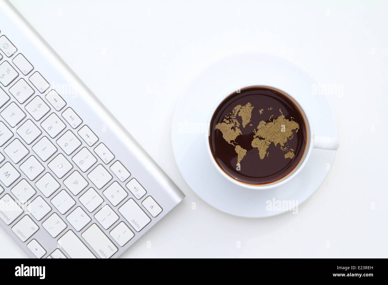 A cup of coffee with its foam formed into a world map presented on white background beside the computer keyboard Stock Photo