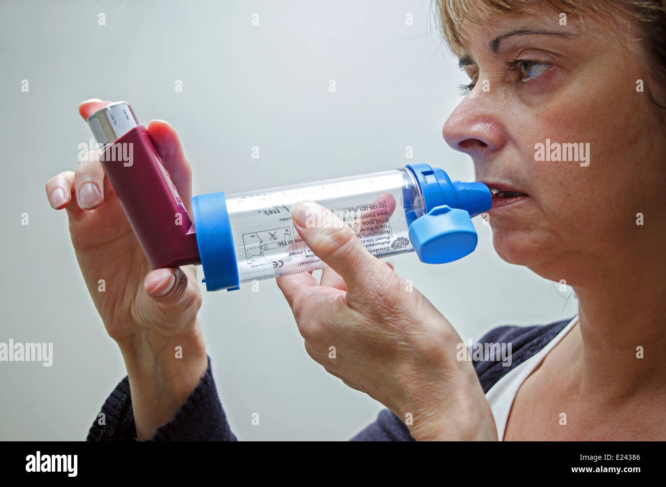 a middle aged woman using an asthma inhaler with spacer to alleviate symptoms Stock Photo