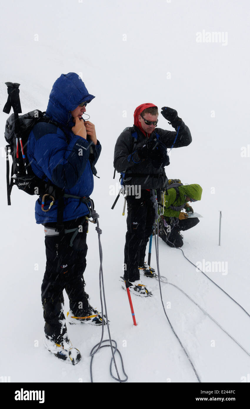 Three mountaineers - two clients wait as the guide kneels and map reads in a white-out on Wildstrubel in the Swiss Alps Stock Photo