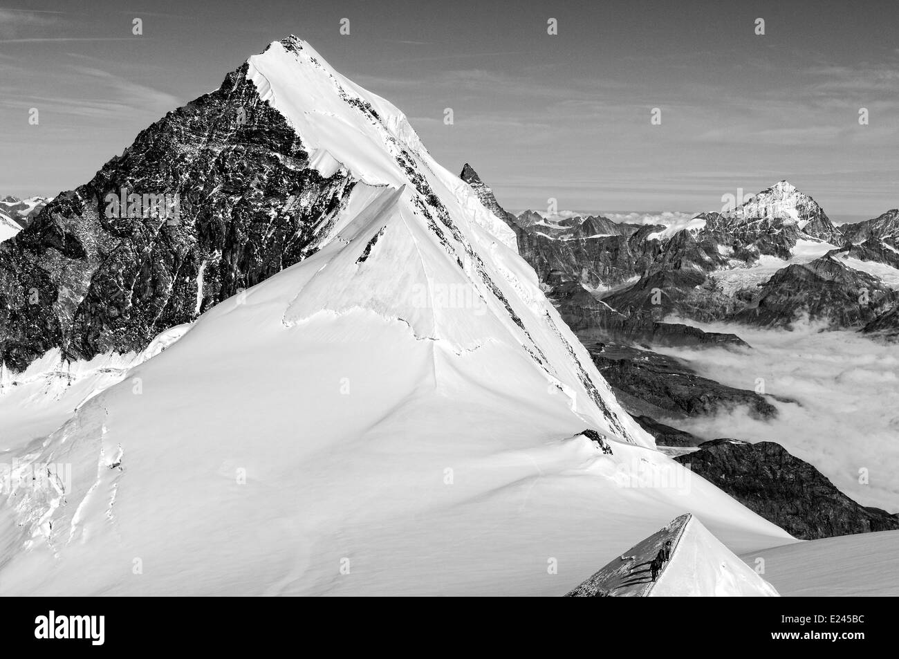 Mountaineers on a narrow ridge high on Monte Rosa, Swiss alps with the north face of Lyskamm to the left & Weisshorn on horizon Stock Photo