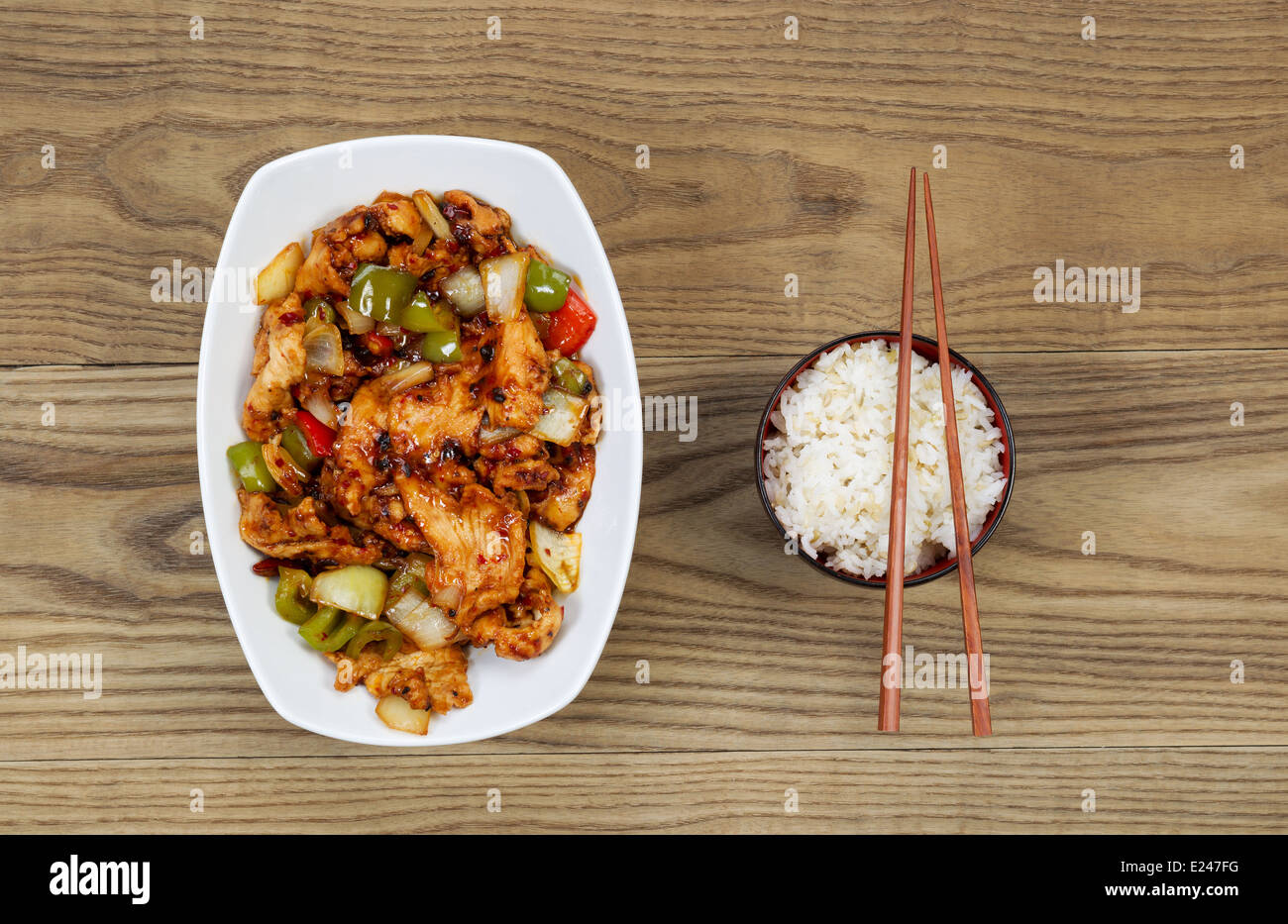 Overhead view of Chinese spicy chicken dish and rice in bowl with chopsticks placed on rustic wooden boards. Stock Photo