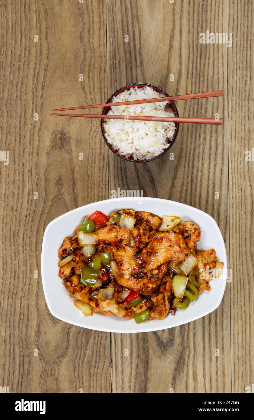 Vertical overhead view of Chinese spicy chicken dish and rice in bowl with chopsticks placed on rustic wooden boards. Stock Photo