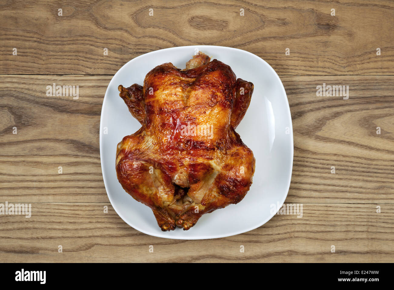 Overhead view of a freshly oven roasted whole chicken in white serving plate placed on rustic wood Stock Photo