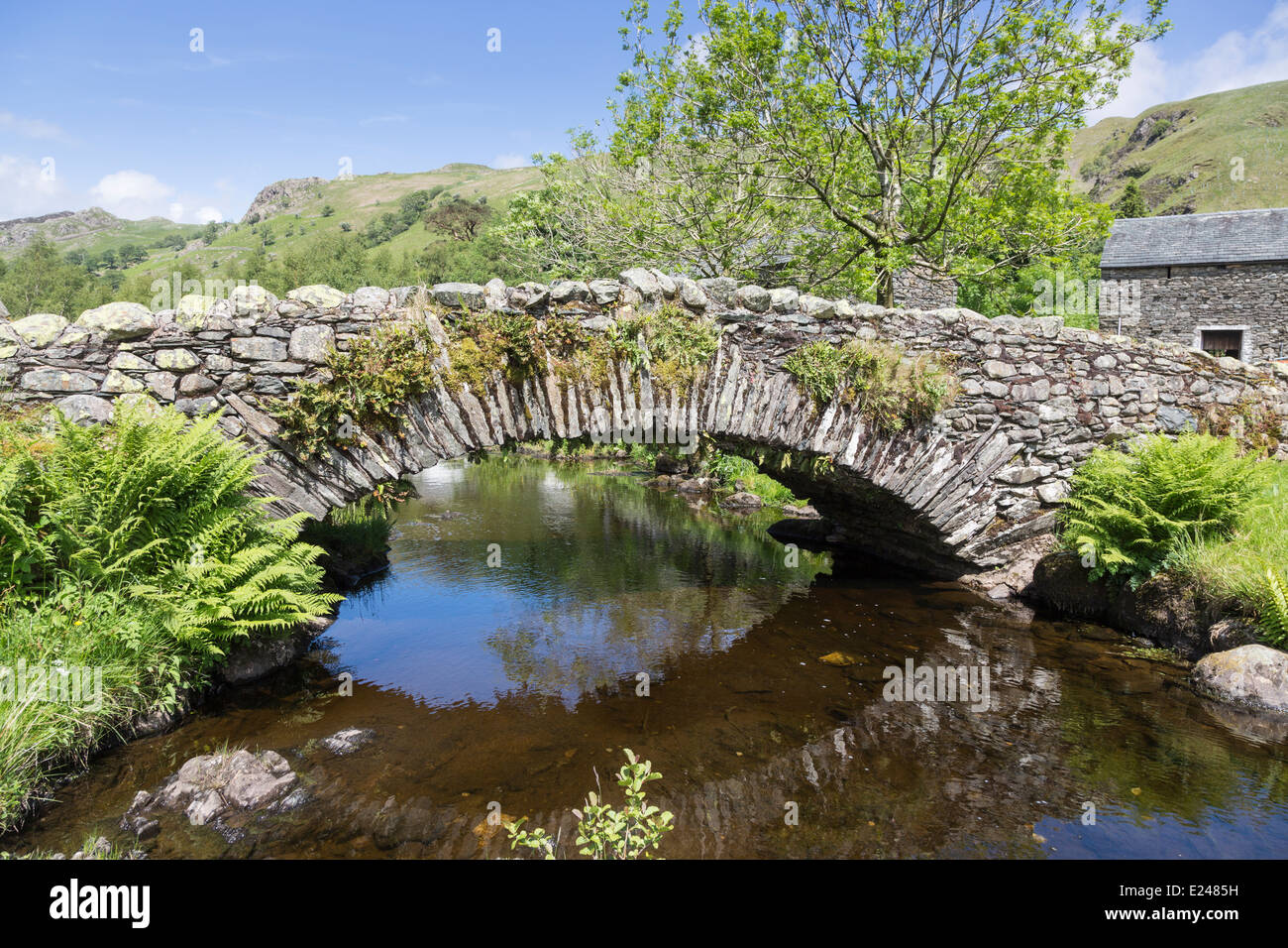Traditional stone bridge with reflection in stream at Watendlath, Borrowdale, Lake District, Cumbria, UK, blue sky in summer Stock Photo