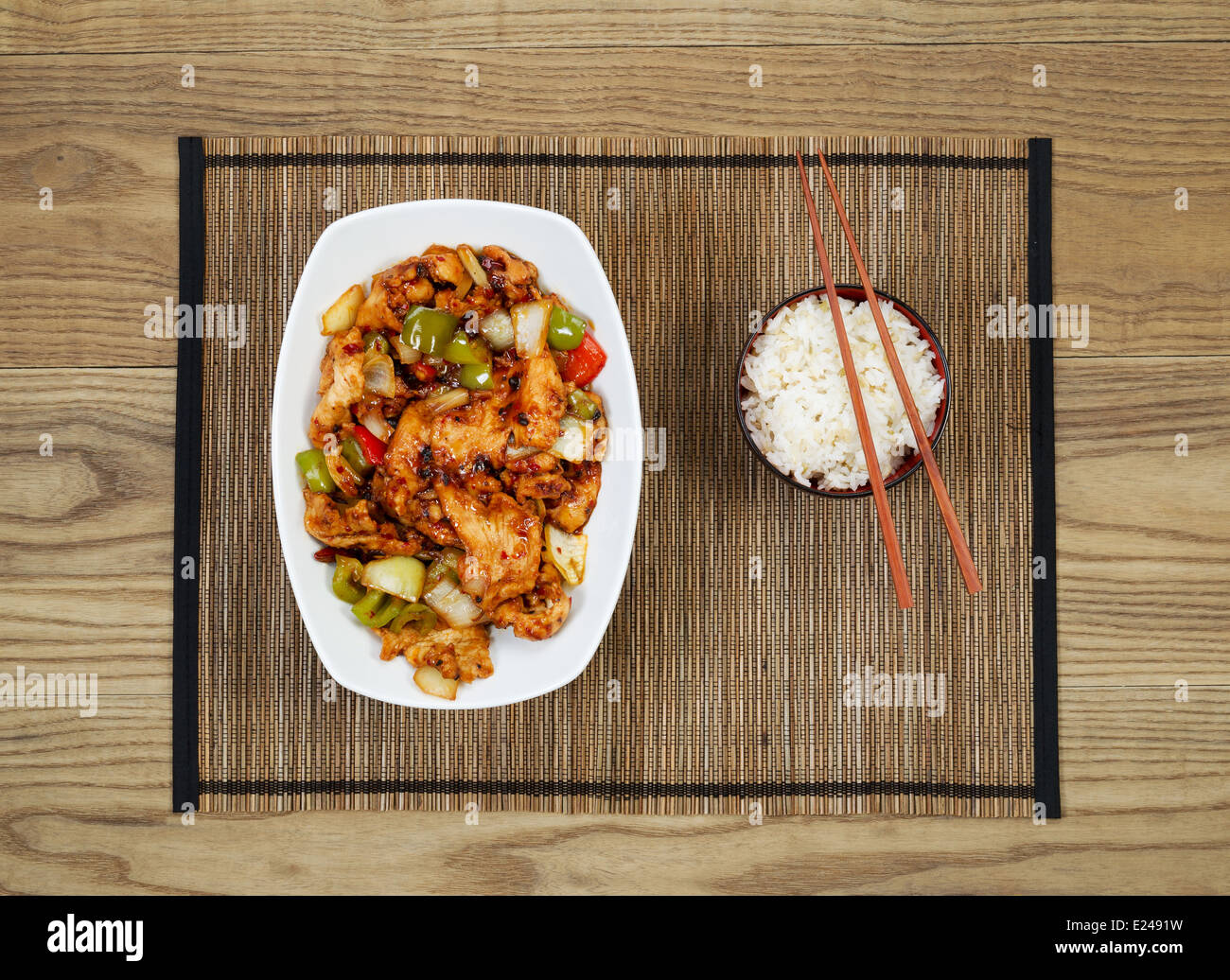 Overhead view of Chinese spicy chicken dish and rice in bowl with chopsticks placed on natural bamboo mate with rustic wooden Stock Photo