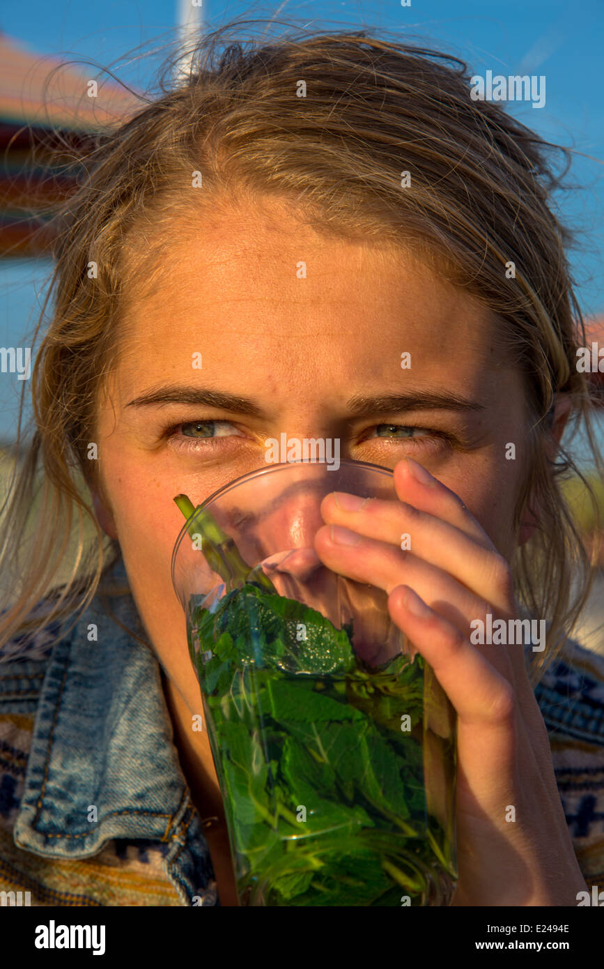a blond and pretty young woman drinking mint tea on a terrace in the sun Stock Photo