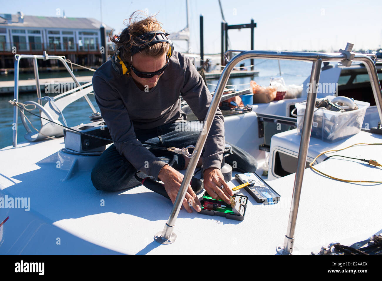A male works on the deck of his boat wearing headphones listening to