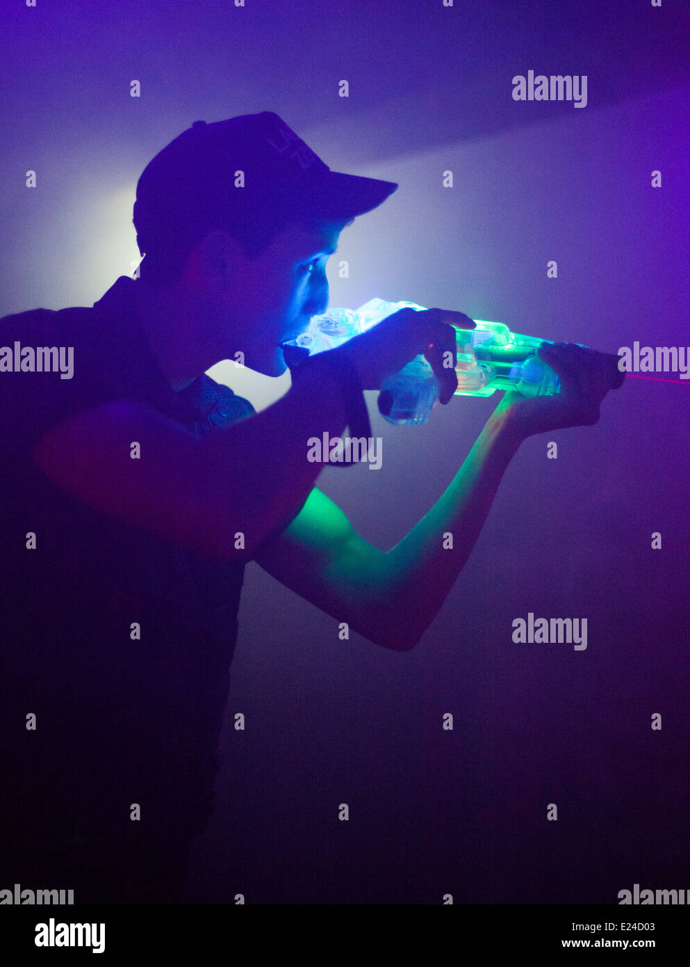 a male model playing a laser / lazer gun war game in a special darkened arena under UV lighting with light beams Stock Photo