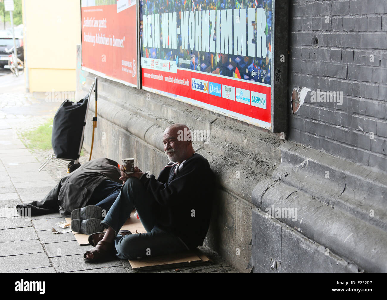 Berlin, Germany. 13th June, 2014. A homeless man from Bratislava sits in front of a placard reading 'Your World Cup living room' under a bridge at Friedrichstrasse station in Berlin, Germany, 13 June 2014. The slogan promotes the public viewing event at Alte Foersterei stadium in Berlin. Photo: Stephanie Pilick/dpa/Alamy Live News Stock Photo
